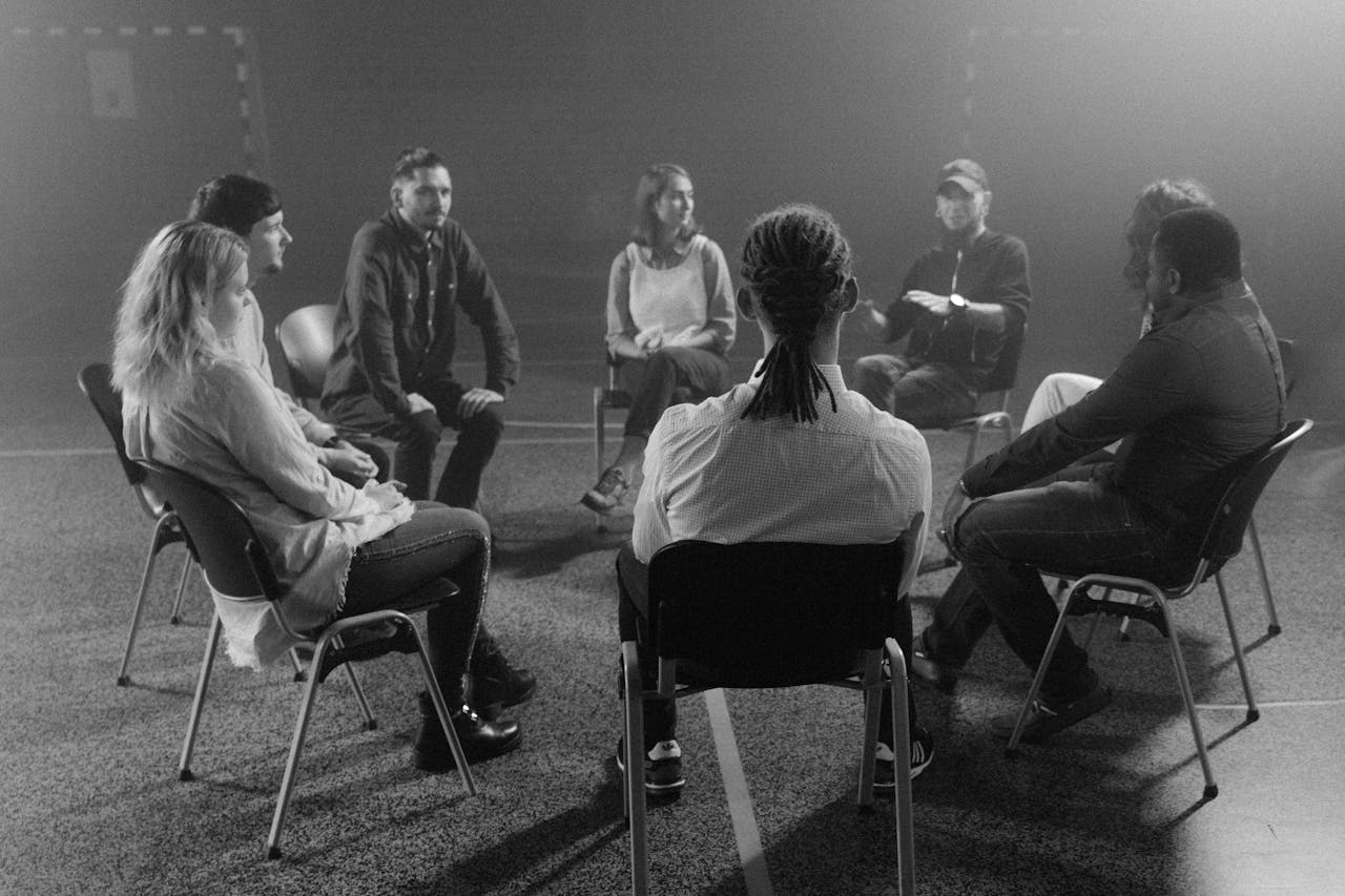 Services A diverse group of people in a circle discussing and supporting each other in a therapy session.