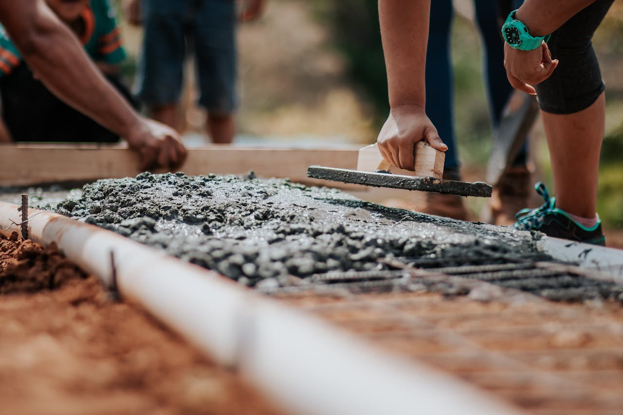 About Construction workers leveling fresh cement on a sunny day at an outdoor site.